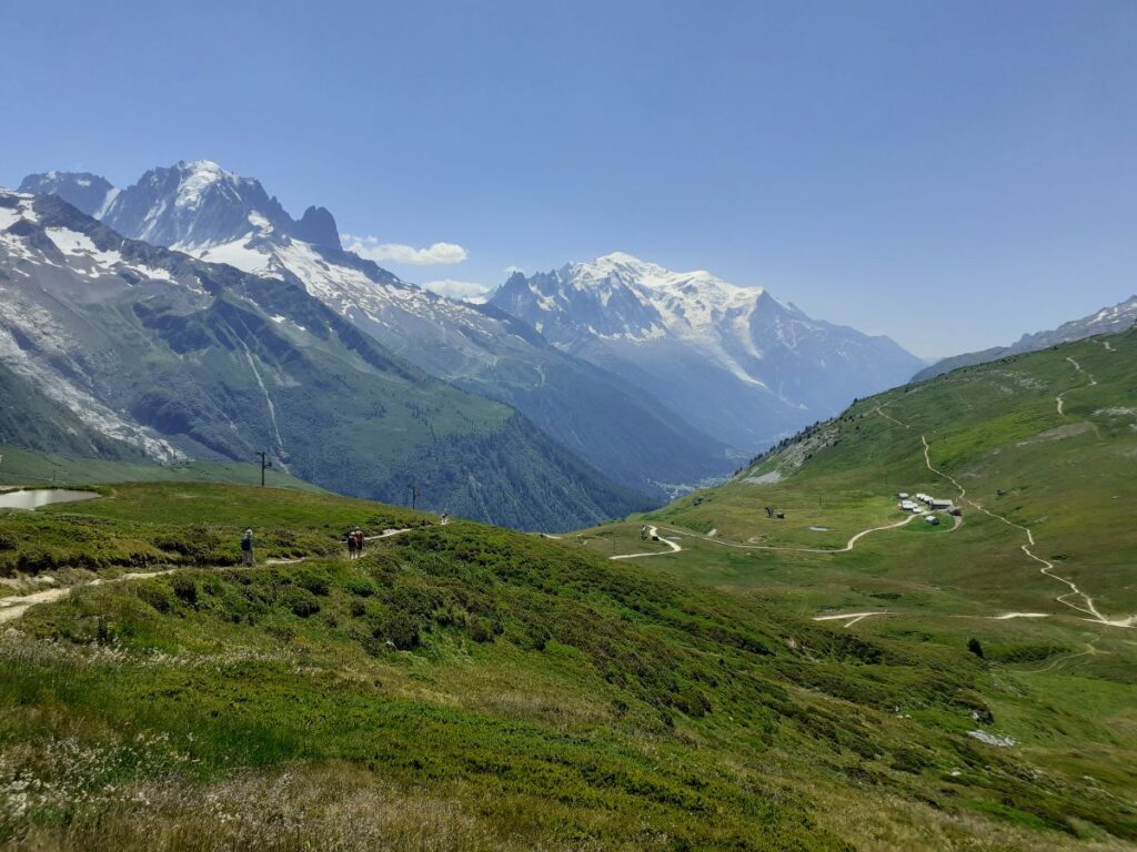 Mountain landscape with green hills and winding paths beneath snow-capped peaks